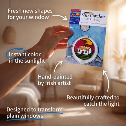 A hand holds a packaged 'Sun Catcher' sticky bead against a softly blurred warm interior background. The product card shows a round window sticker with a house and sun design, and multiple callout text overlays describe the product features and benefits.