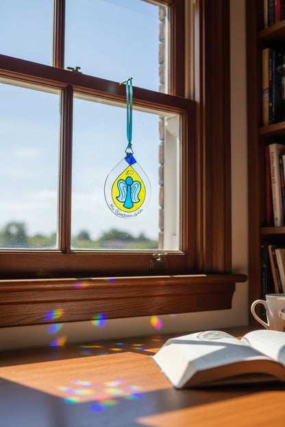 A clear glass suncatcher ornament shaped like a teardrop, featuring a yellow center with a blue and light blue angel design, a blue diamond-shaped accent, and a teal ribbon loop at the top. Handwritten text at the bottom reads 'My Guardian Angel'.
