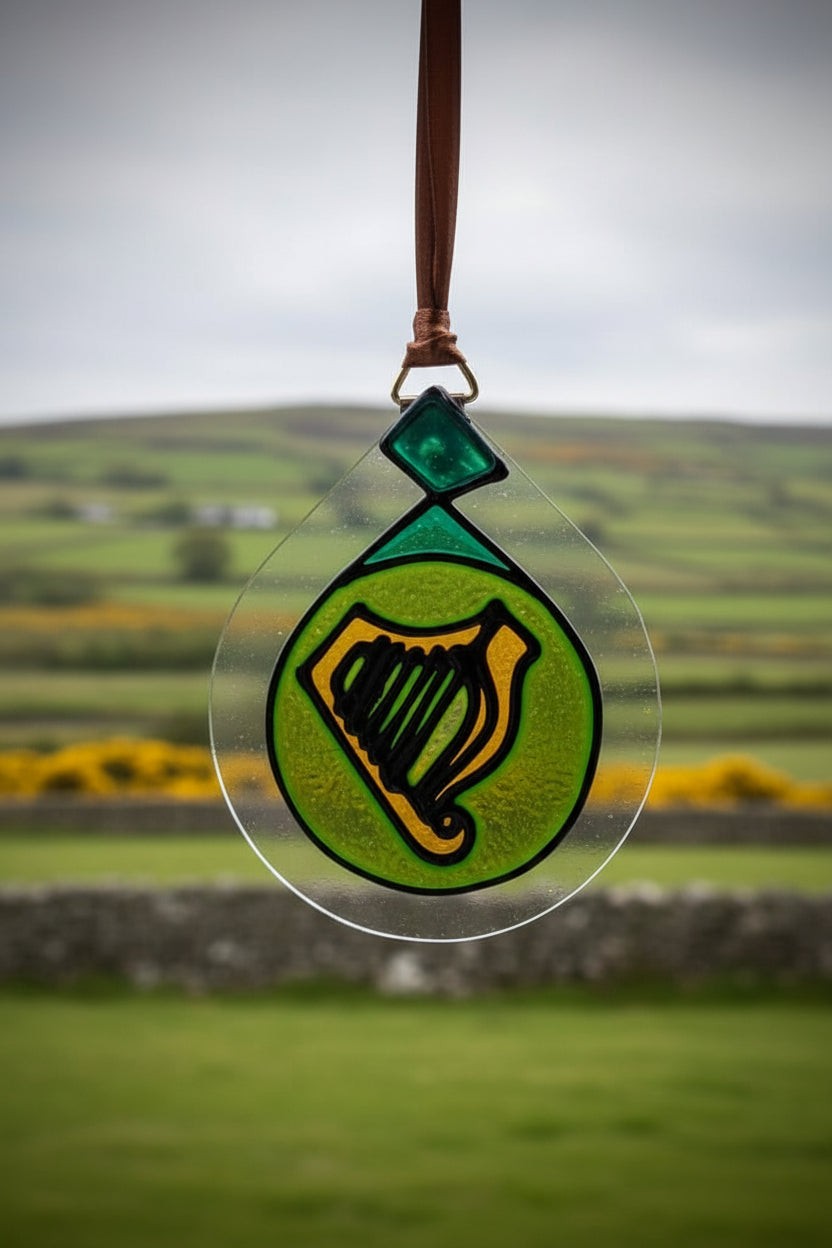 A stained glass ornament featuring a green harp on a bright green circular background, suspended by a brown ribbon against a white wall.
