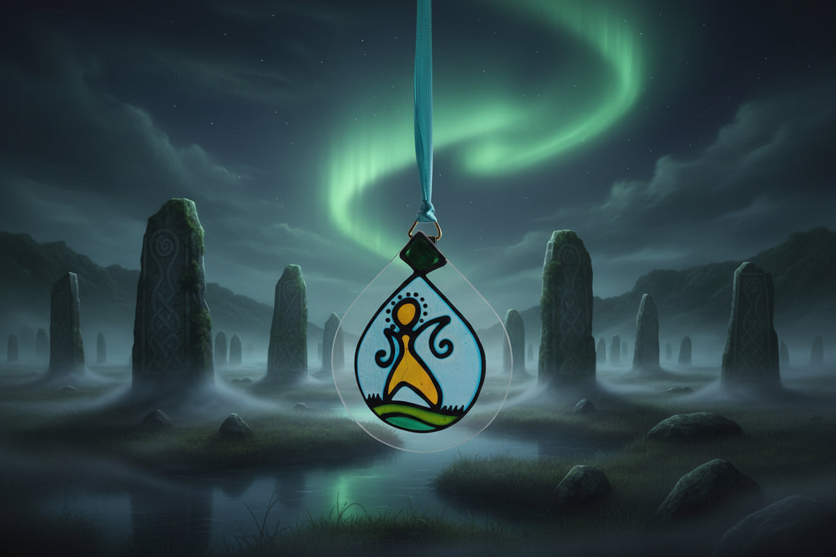 A teardrop-shaped stained glass hanging ornament with a blue ribbon, featuring a stylized figure in yellow and orange on a light blue background with green grass, shown against a white wall.