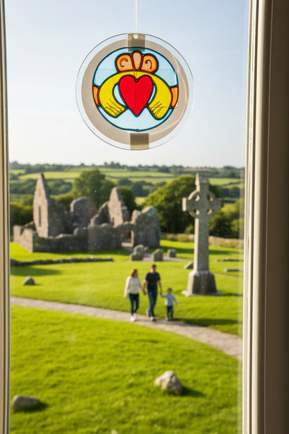 A packaged stained glass sun catcher featuring a Claddagh design with two gold hands holding a red heart, mounted on a clear circular frame and attached to a printed backing card.