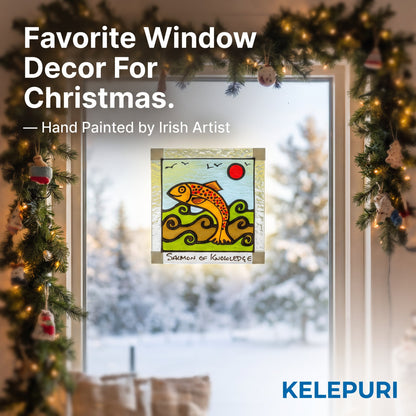 A festive Christmas-themed promotional image showing a hand-painted stained glass window panel depicting a gold fish on green waves under a red sun, mounted on a window with a snowy outdoor view behind it. The window is framed by a decorated green pine garland with warm string lights.