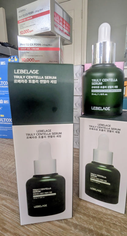 LEBELAGE Truly Centella Serum shown with its green and white retail box, a dark green bottle with a silver dropper cap, and two additional product boxes stacked in the background on a tabletop.